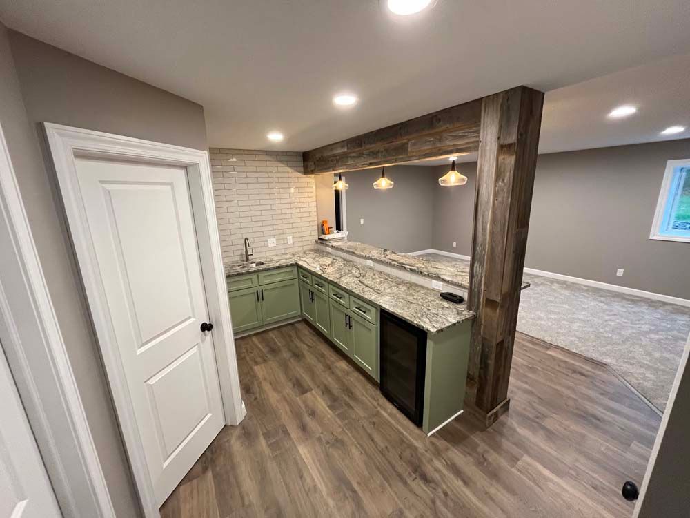 Empty kitchen with green cabinets, granite island, wood flooring, and recessed lighting in an open-plan room