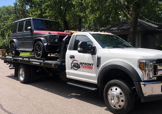 Tow truck hauling a black SUV on a flatbed in a sunny residential street