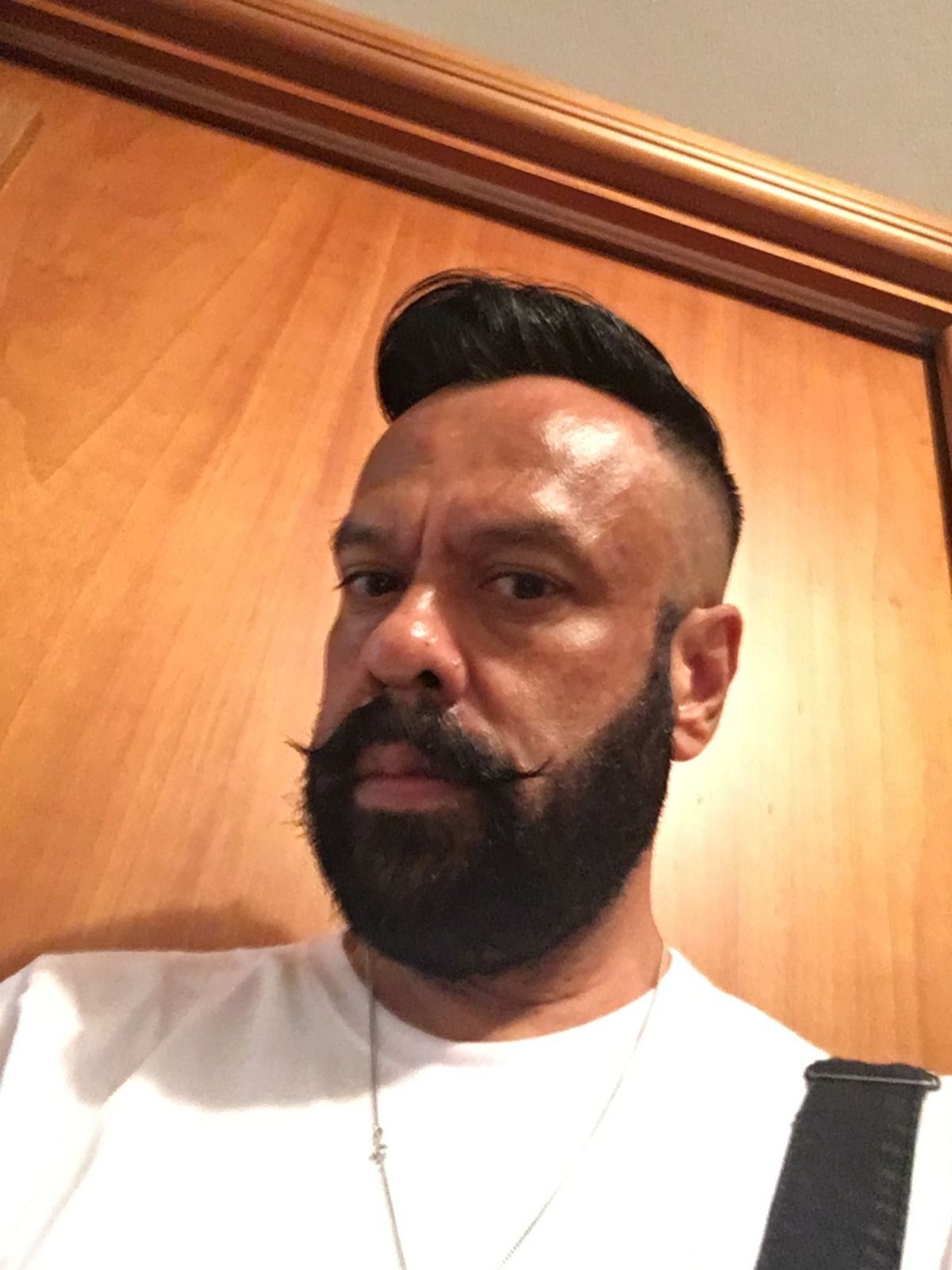 Homem de cabelos e barba escuros, vestindo camisa branca, olhando para a câmera.