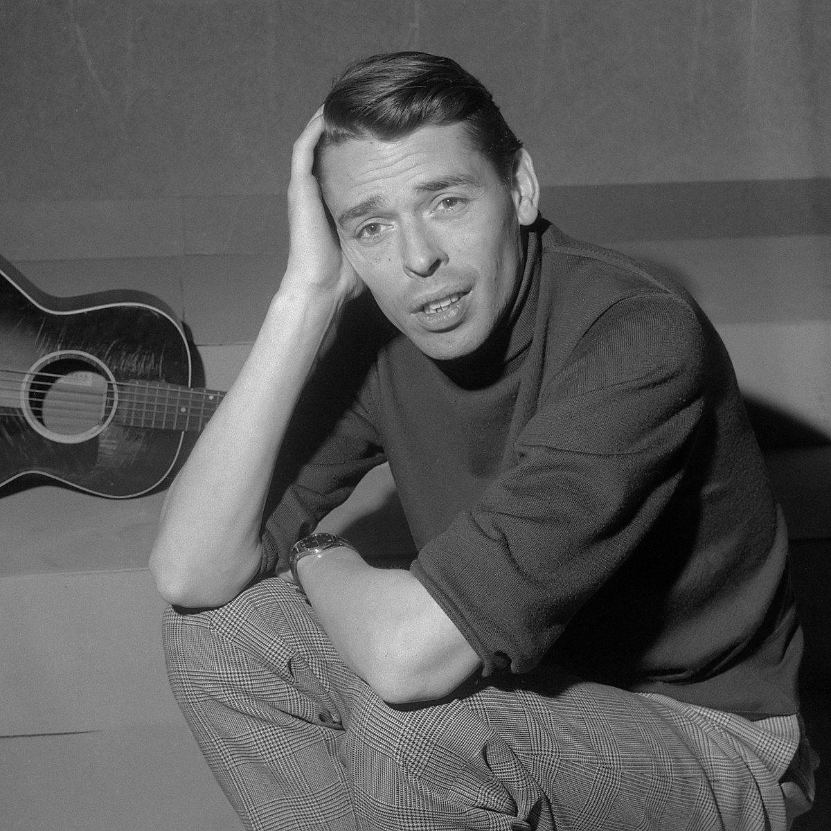 Een zwart-witfoto van een man die naast een gitaar zit