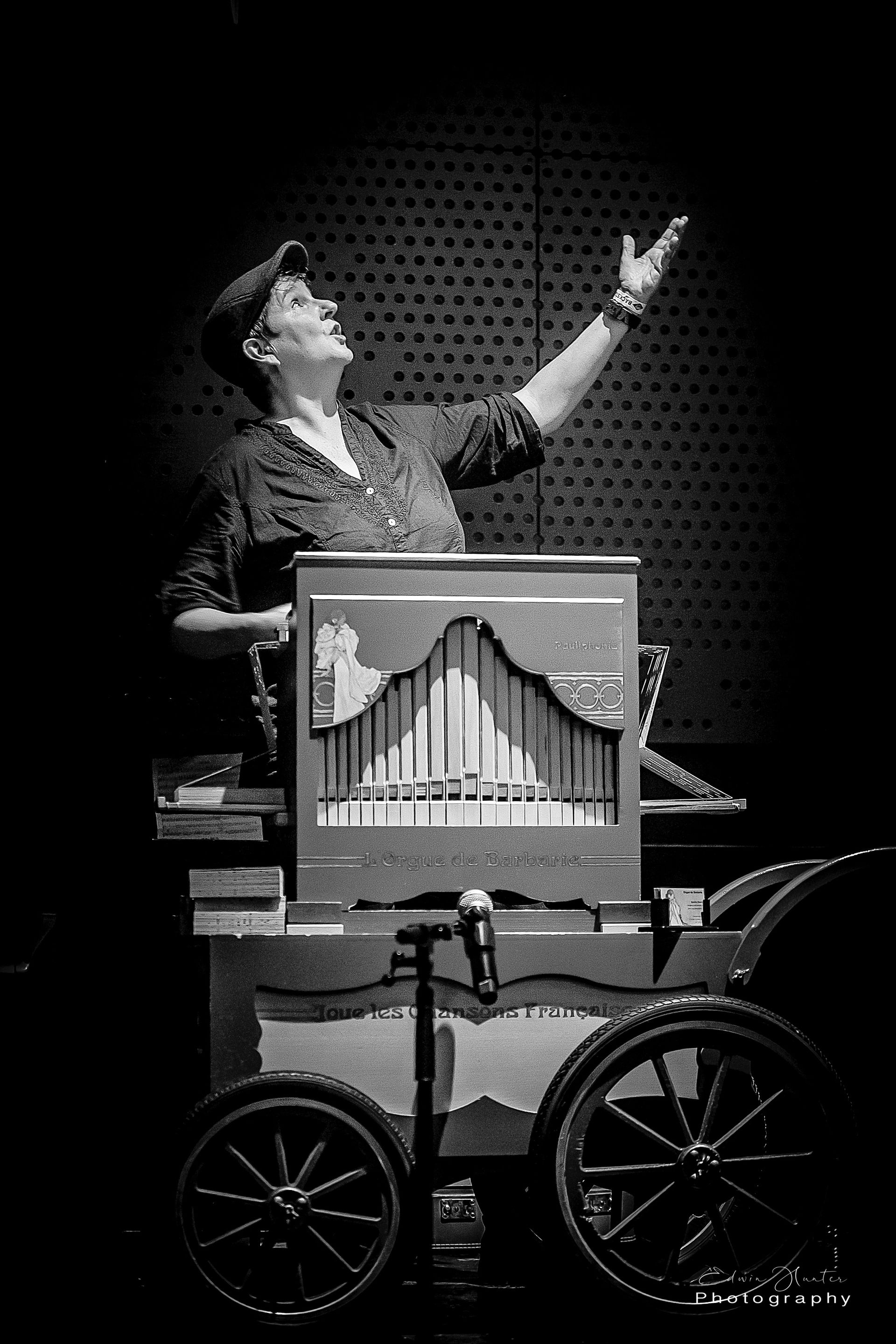 Een vrouw bespeelt een orgel op een kar op een zwart-witfoto.