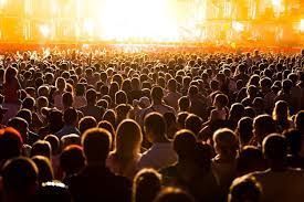 Tijdens een concert zit een grote menigte mensen voor een podium.