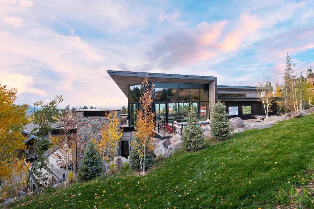 A modern house is sitting on top of a lush green hillside surrounded by trees.