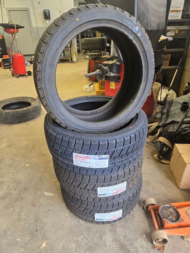 Stacked winter tires in a workshop, with one tire standing upright on top | Auto Care Technical Services Inc.