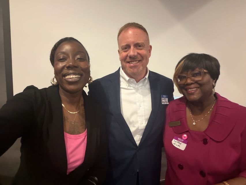 Three people smiling indoors, posing together in business attire.