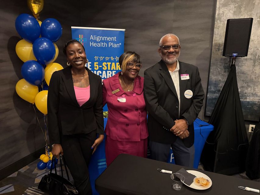Three people posing beside balloons and a blue event sign at an Aetna Health Plan gathering.