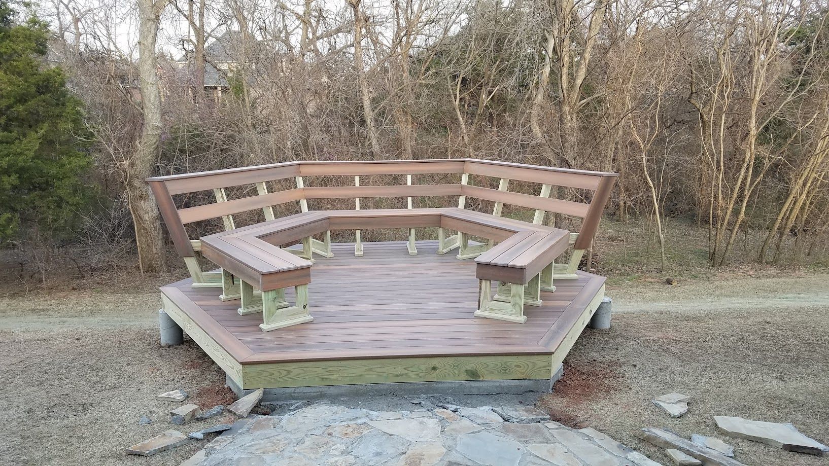 Curved wooden bench around a small platform in a wooded outdoor clearing