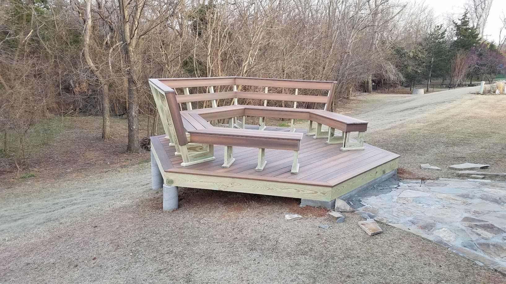 Weathered wooden bench with a low table on a grassy path beside brush and trees