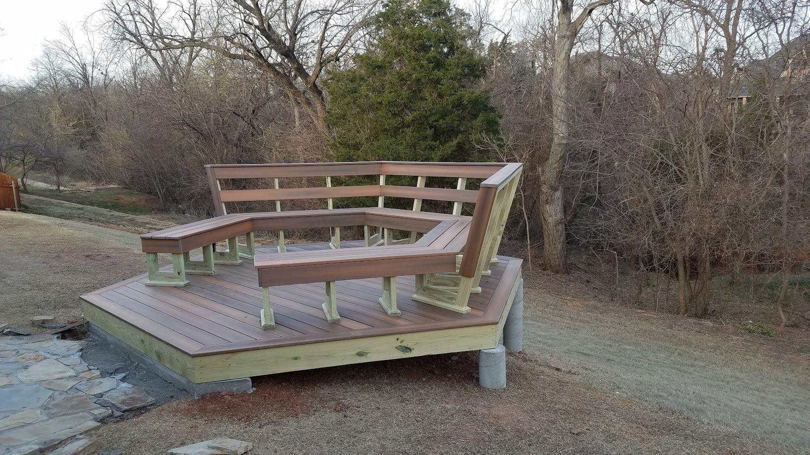 Wooden benches and tables on a small outdoor deck in a grassy, wooded area