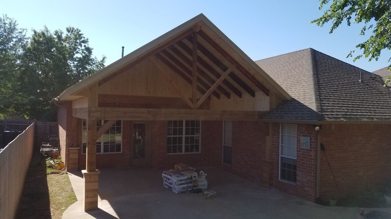Brick house with a covered front porch and triangular wood roof, surrounded by trees.