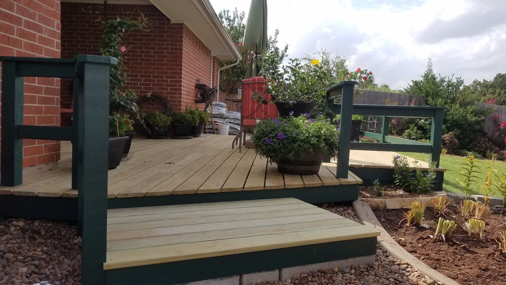 Wooden porch steps leading to a brick house patio with potted flowers and garden beds
