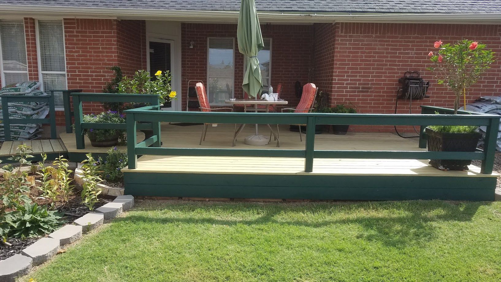 Brick house porch with green railing and patio chairs, front lawn in foreground