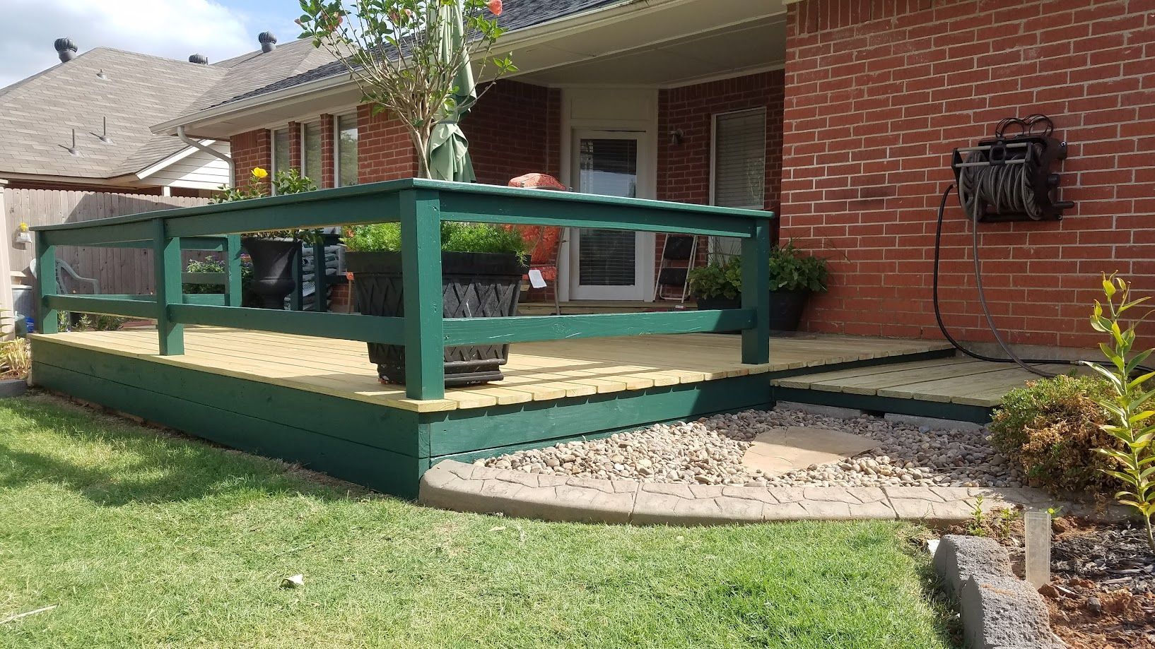 Back porch with green wooden deck railing beside a brick house and lawn