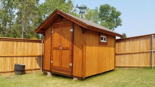 Brown wooden garden shed with double doors in a fenced grassy backyard