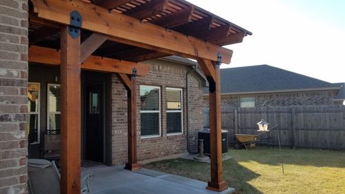 Covered brick patio with wooden posts and a fenced backyard in sunlight