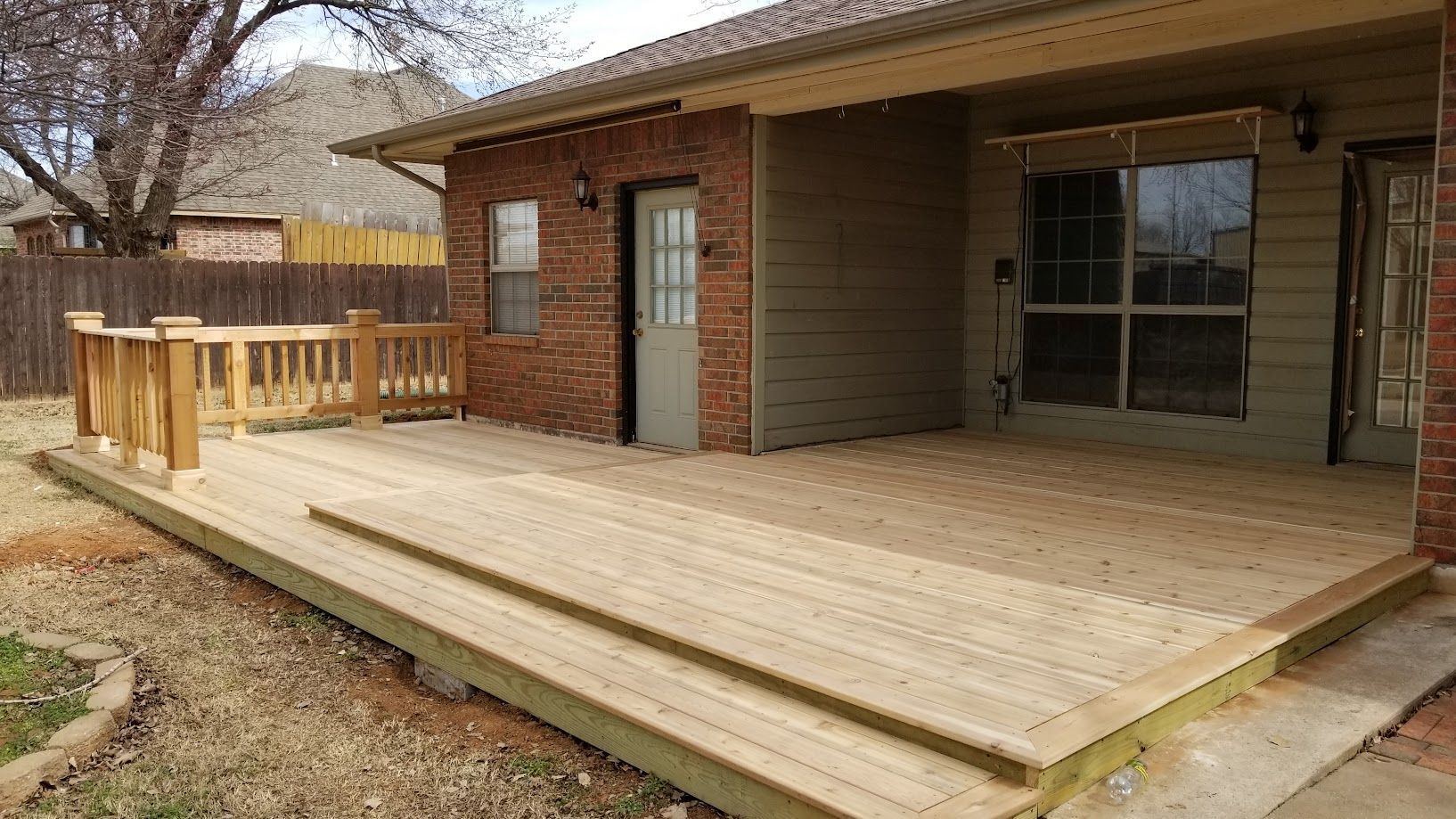 Wooden backyard deck attached to a brick and siding house, with stairs and railing.
