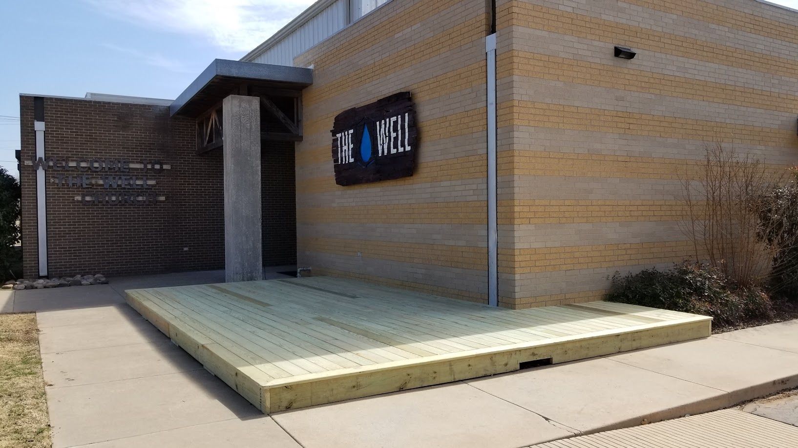 Accessible ramp and entrance platform beside a tan brick building with a blue sign.