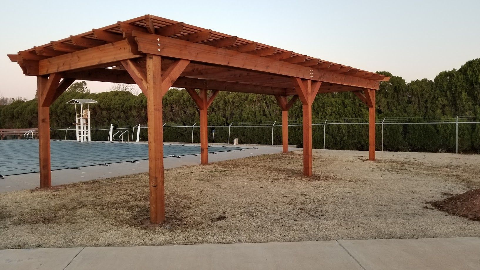 Wooden pergola over gravel beside an empty outdoor pool at sunset