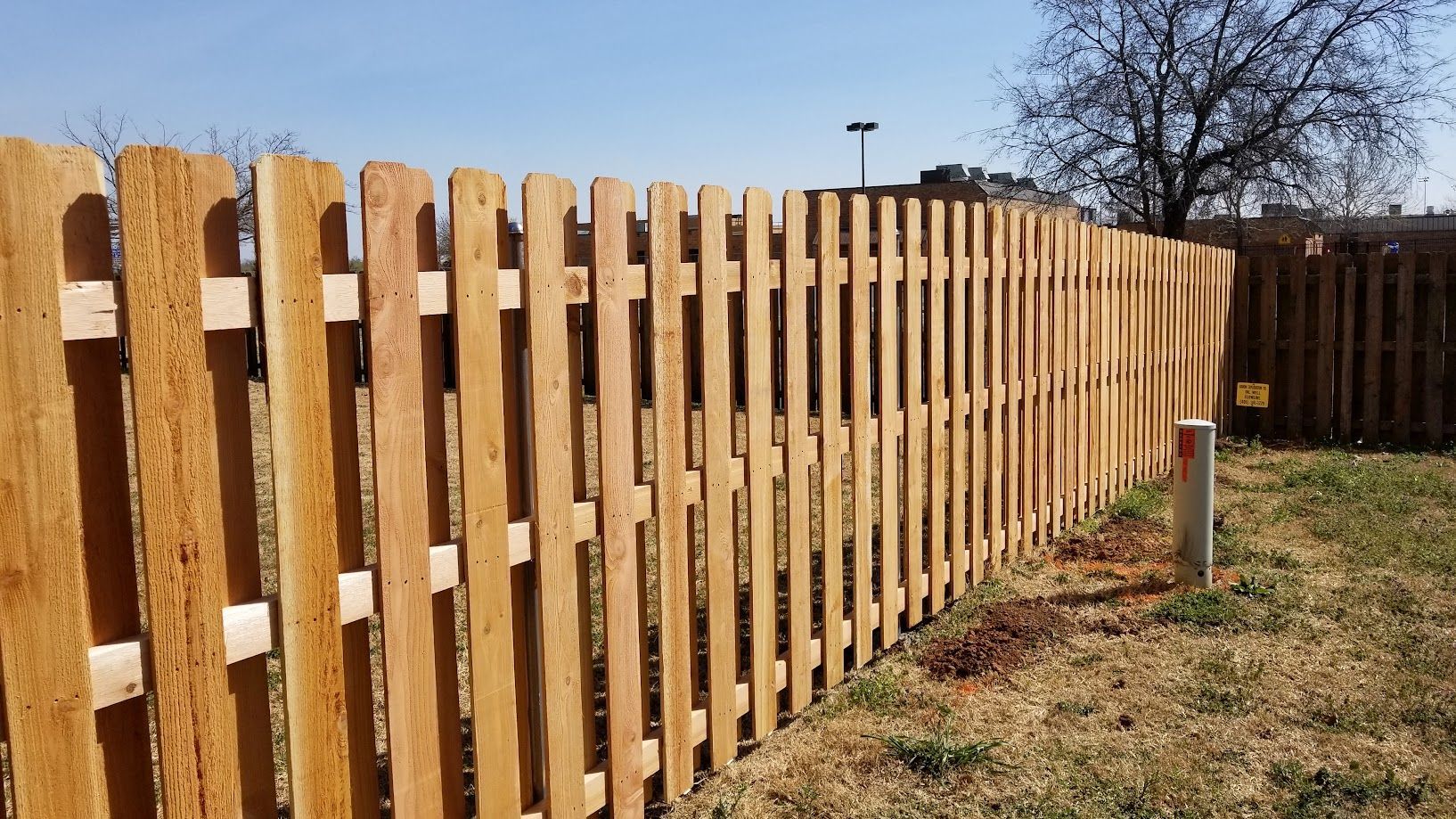 Wooden picket fence along a grassy yard under a clear blue sky