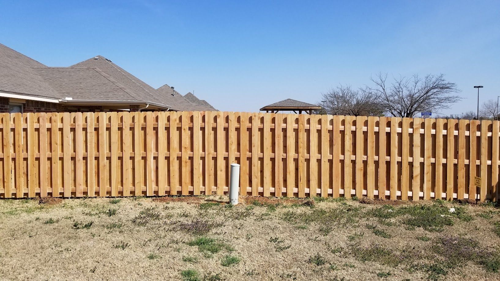 Wooden privacy fence with desert landscaping and a house roofline under a clear blue sky