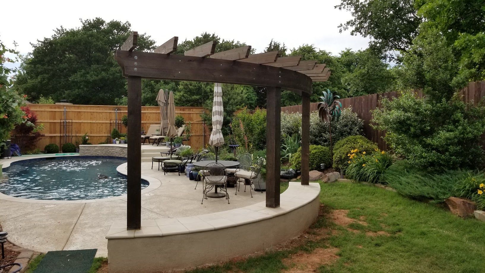 Backyard patio with pergola beside a swimming pool and lush garden greenery