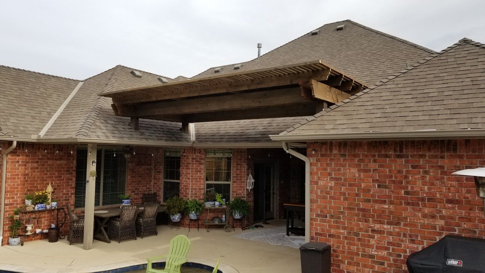 Brick house patio with covered entrance, tan shingle roof, and potted plants