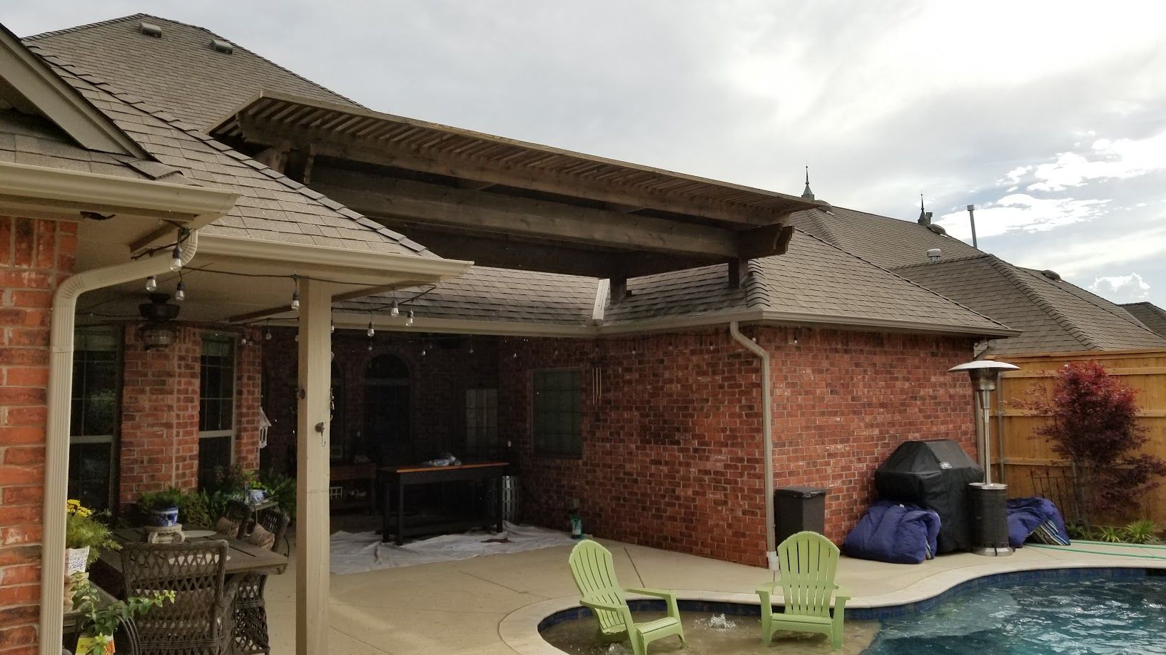 Backyard patio with red brick house, covered seating area, pool, and cloudy sky