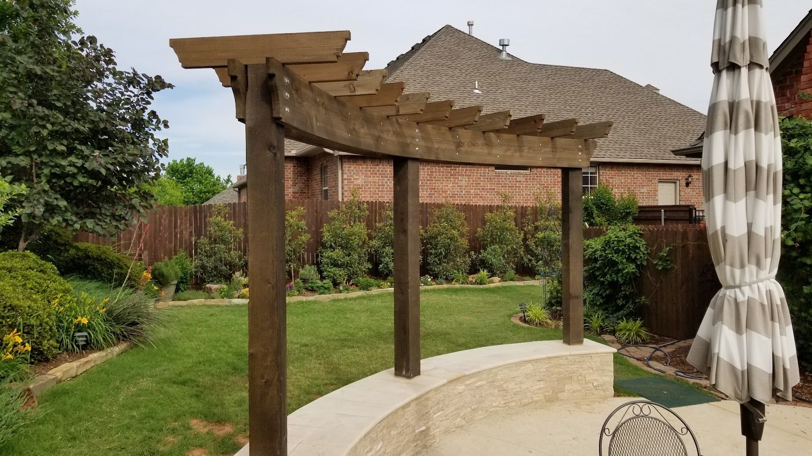 Backyard patio with wooden pergola, stone path, lawn, and closed striped umbrella