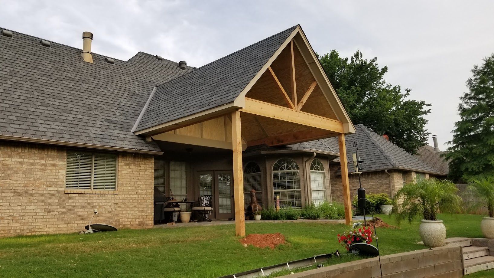 Stone house with a large wooden portico, gray roof, and landscaped lawn under an overcast sky