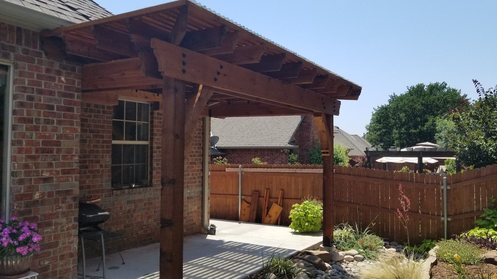 Brick patio beside a house with a wooden pergola and fenced yard in bright sunlight