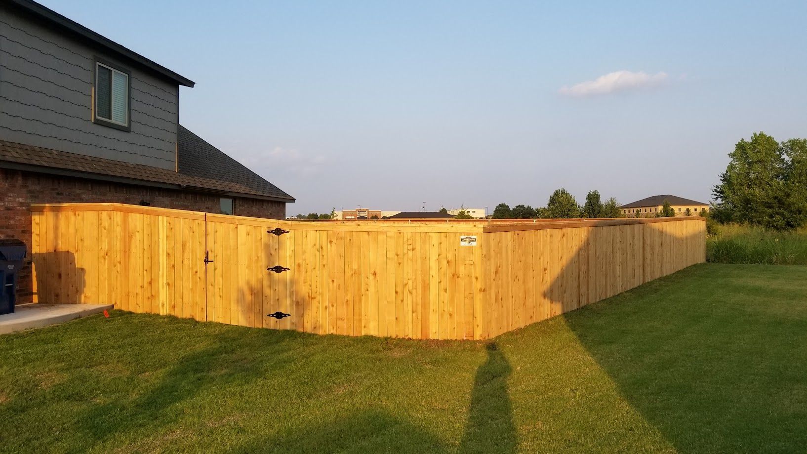 Wooden privacy fence around a backyard lawn beside a house at sunset.