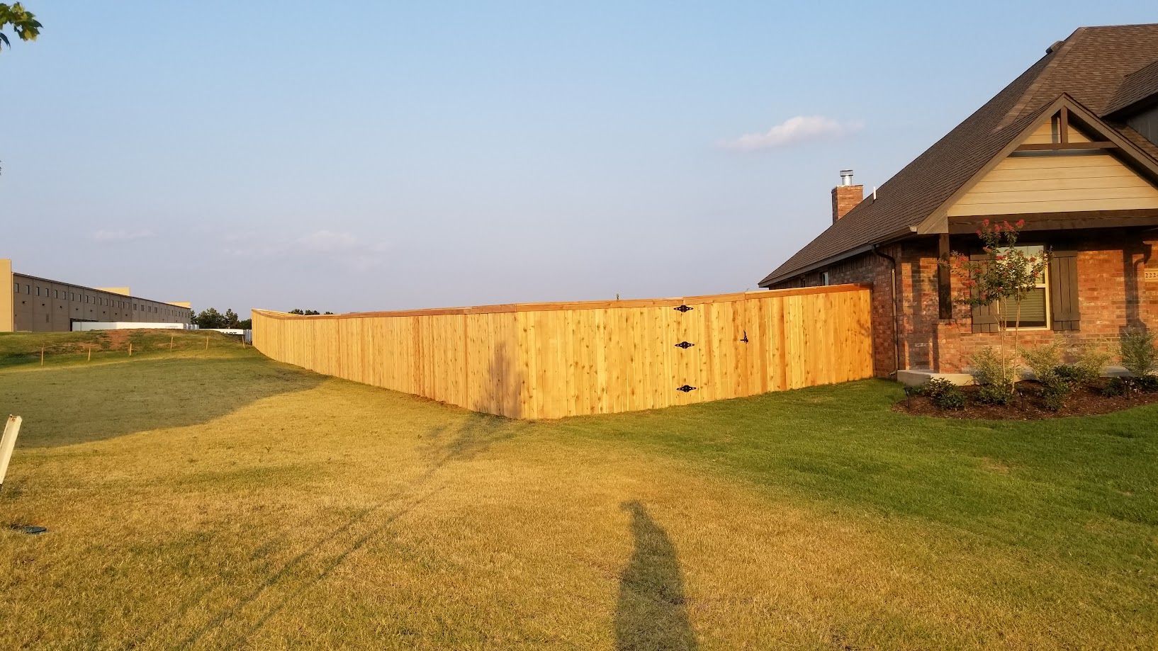 Backyard with long wooden fence beside a brick house at sunset