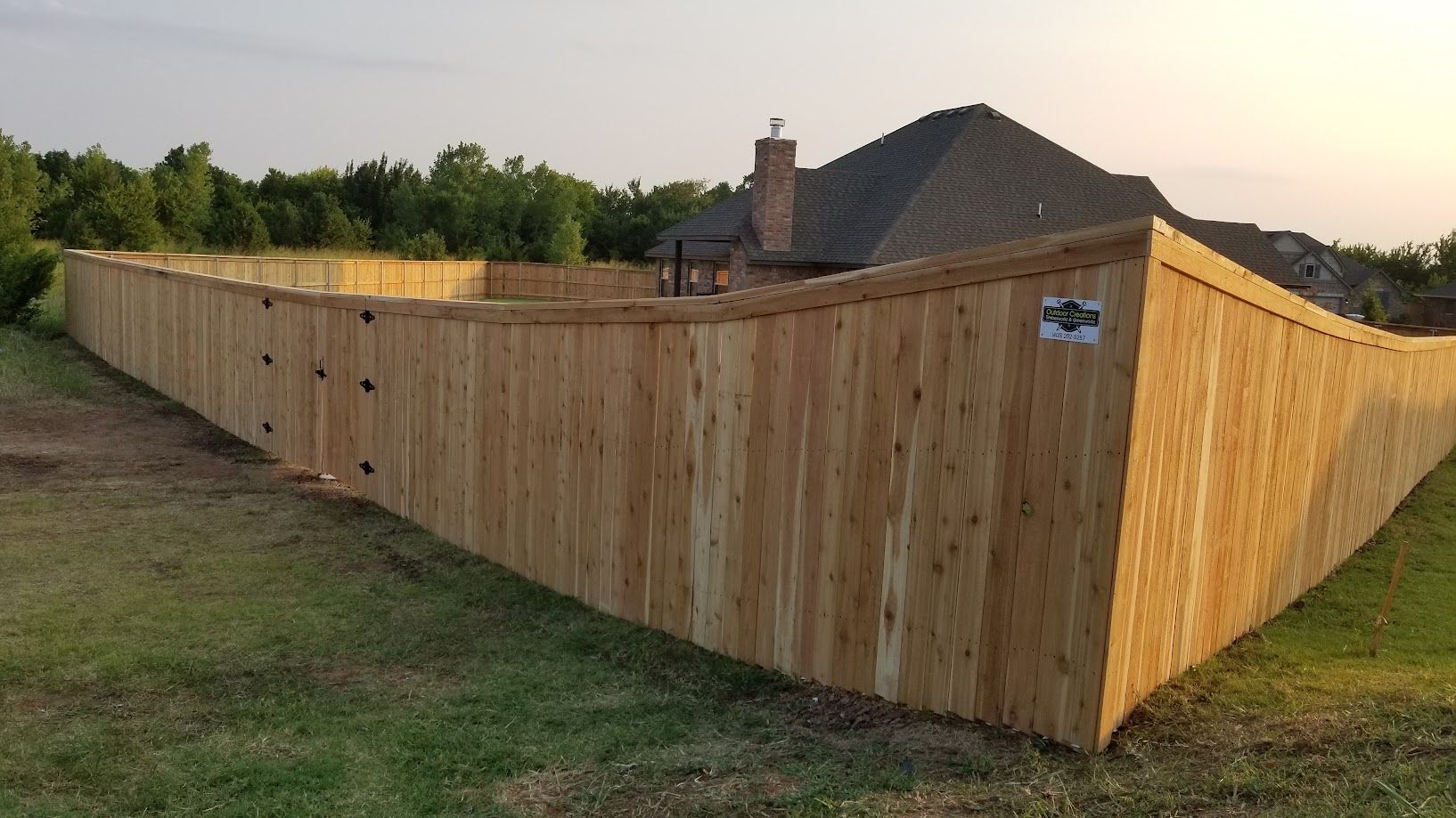 Wooden privacy fence enclosing a backyard beside a house at sunset