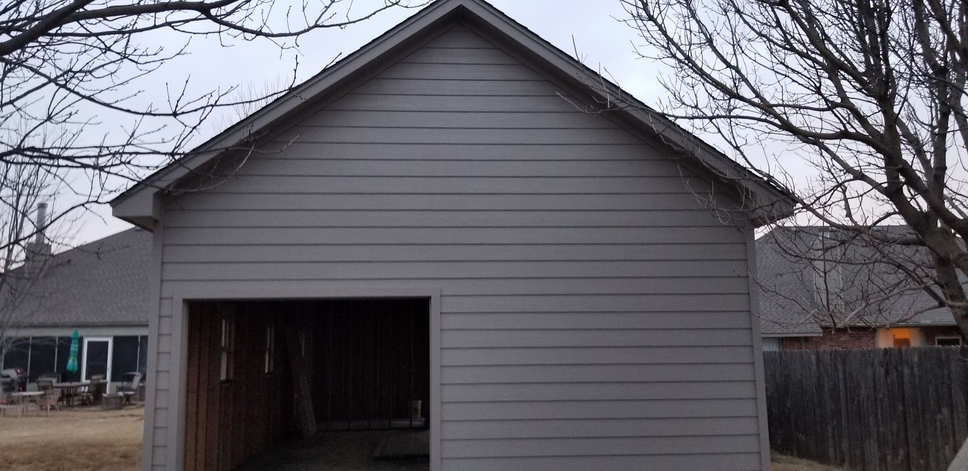 Gray garage with open door and bare trees in the background