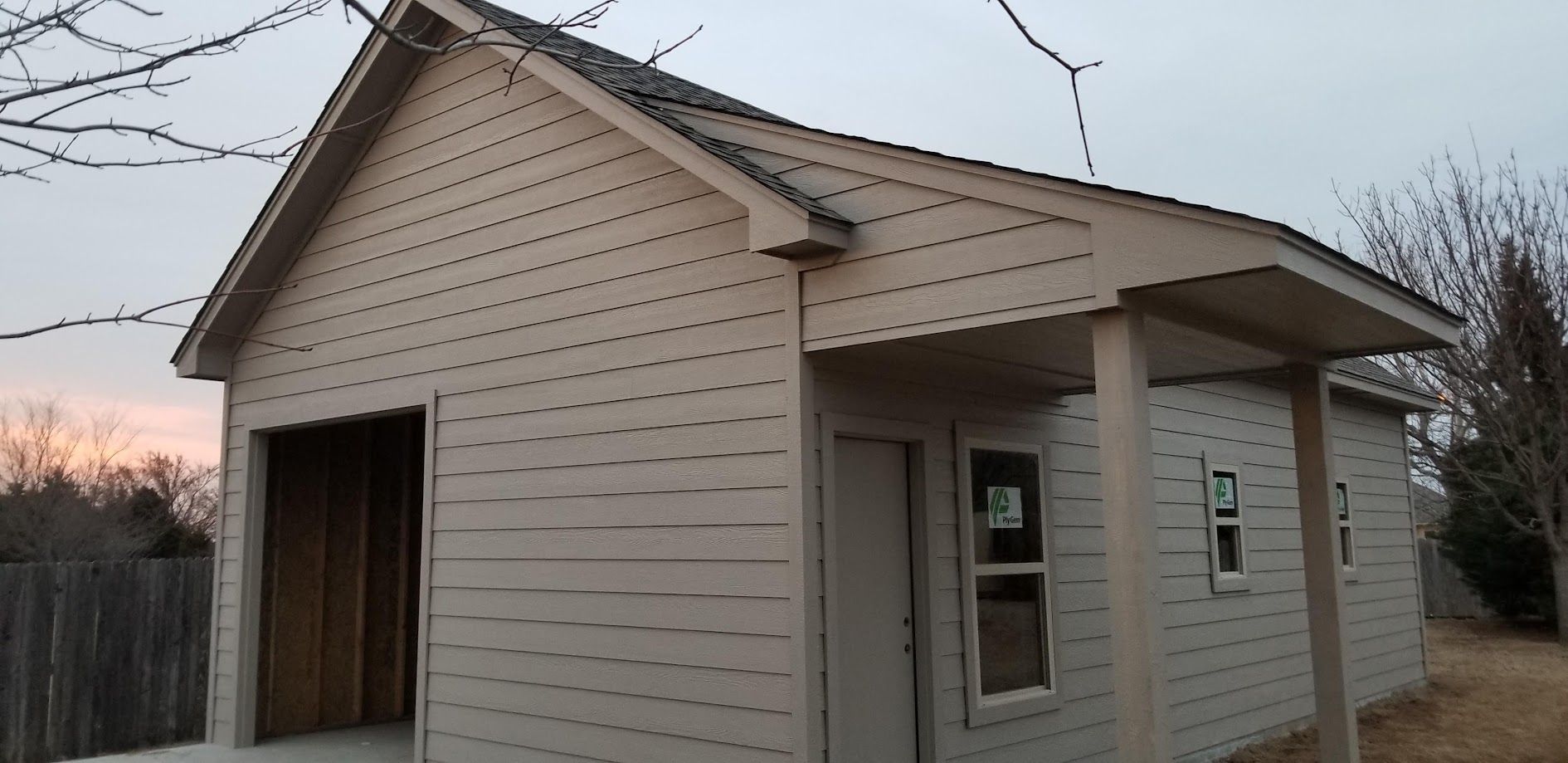 Small beige shed with a gabled roof and open doorway at dusk.
