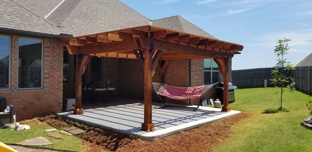 Wooden patio gazebo with a hammock beside a brick house on a sunny lawn