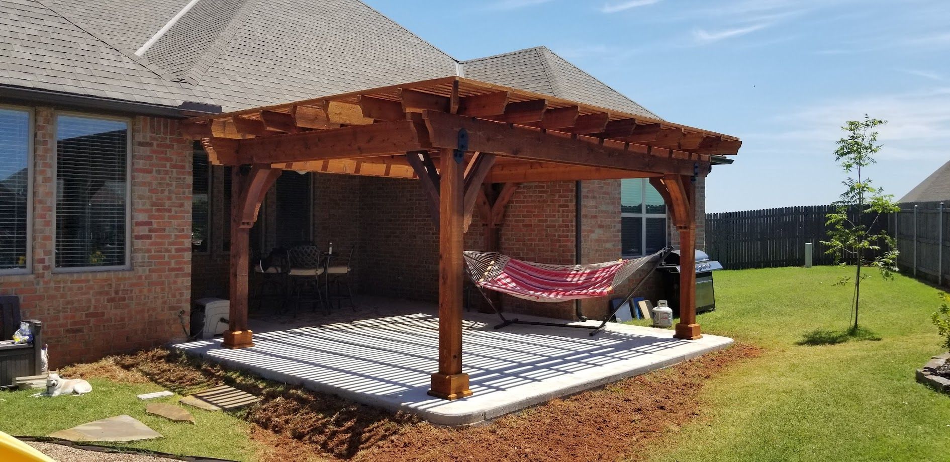 Backyard patio with wooden pergola, hanging hammock chairs, and patterned flooring beside a brick house