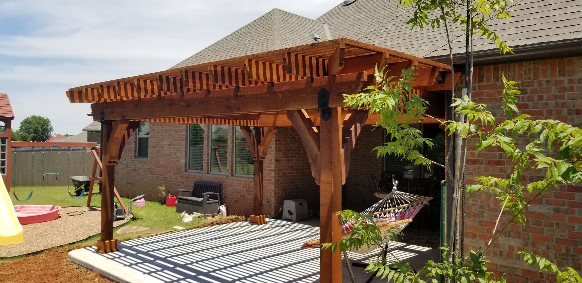 Backyard patio with wooden pergola, brick house, and lounge chairs in a sunny garden