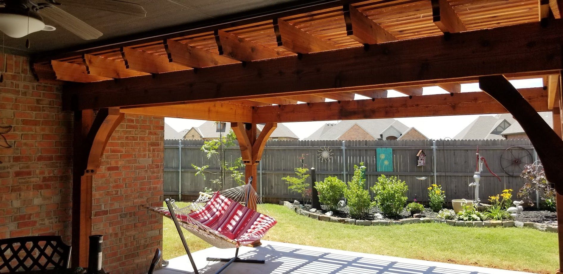 Patio with a striped chair under a wooden pergola, overlooking a sunny garden and stone wall