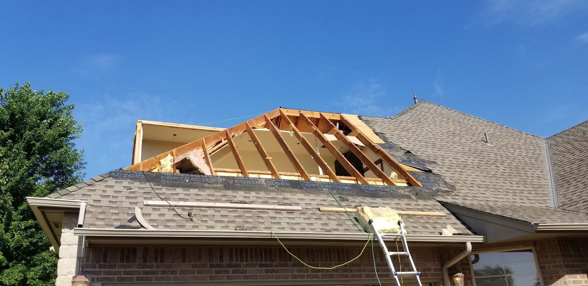 Roof under construction with exposed wooden trusses and a ladder on a suburban house