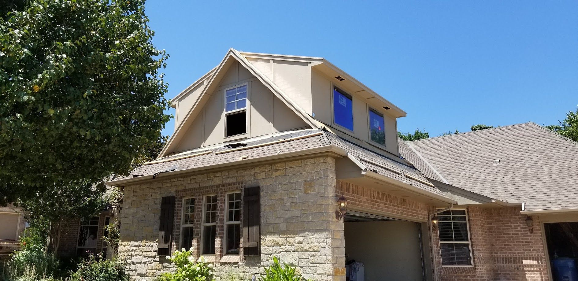 Stone house with beige roof and blue dormer windows under a clear blue sky