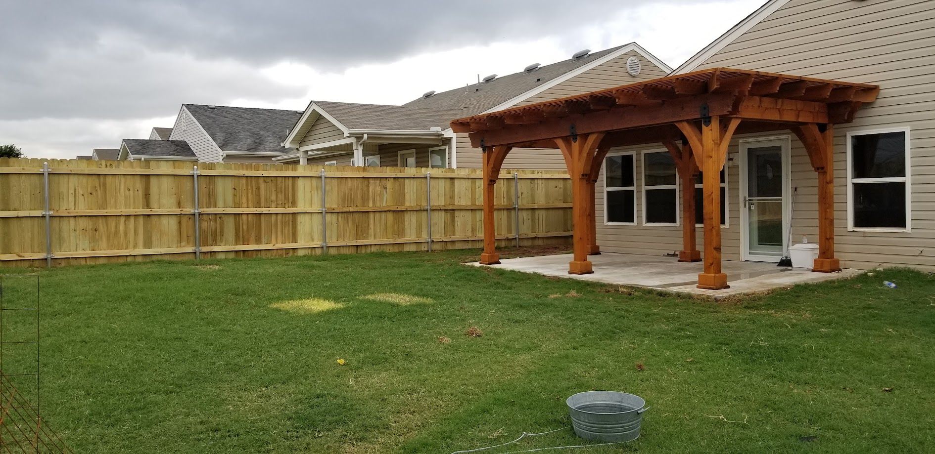Backyard with green lawn, wooden fence, stone patio, and a wooden pergola beside a house