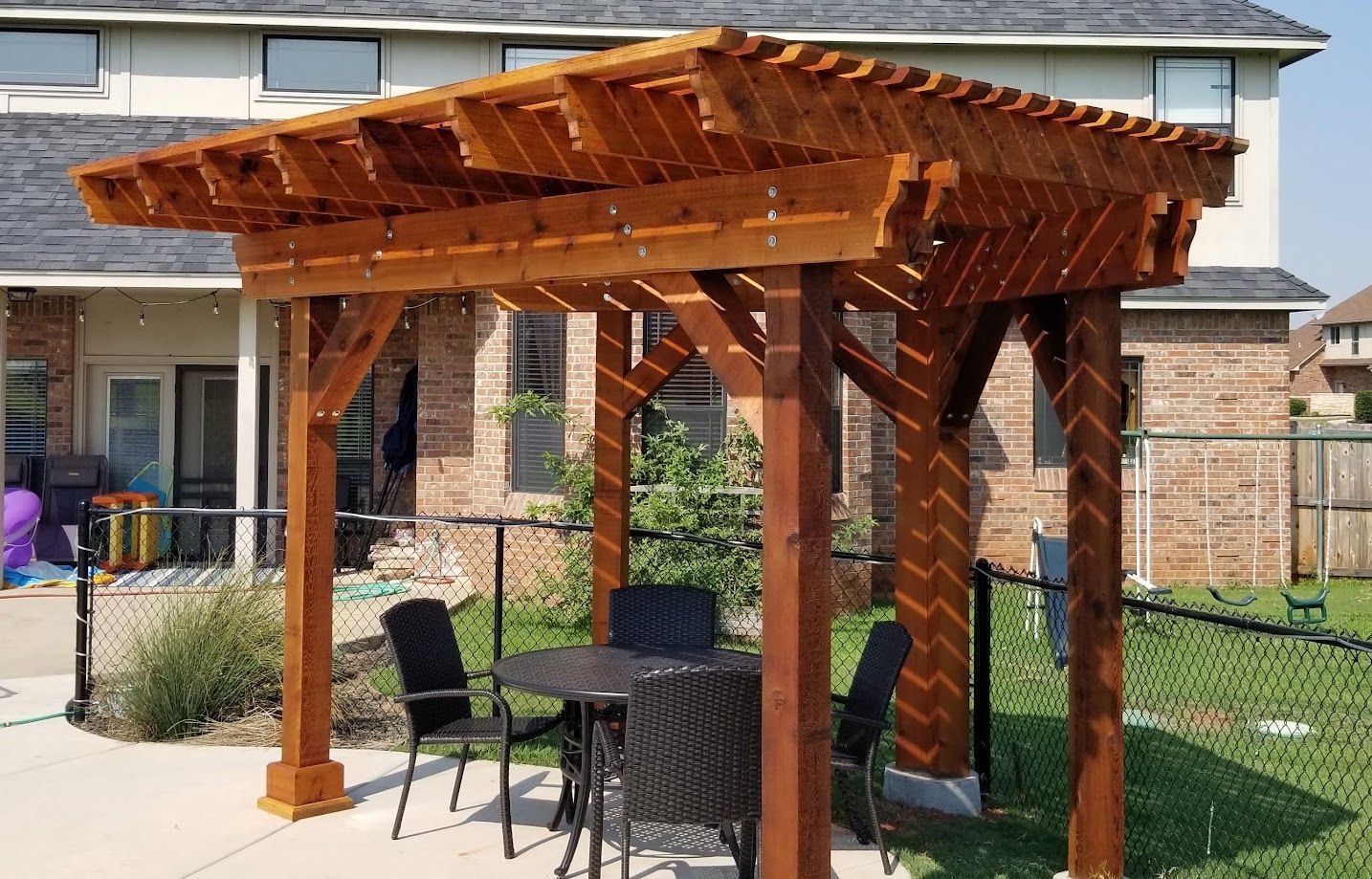 Wooden pergola shading a small patio with chairs and a table in a backyard garden