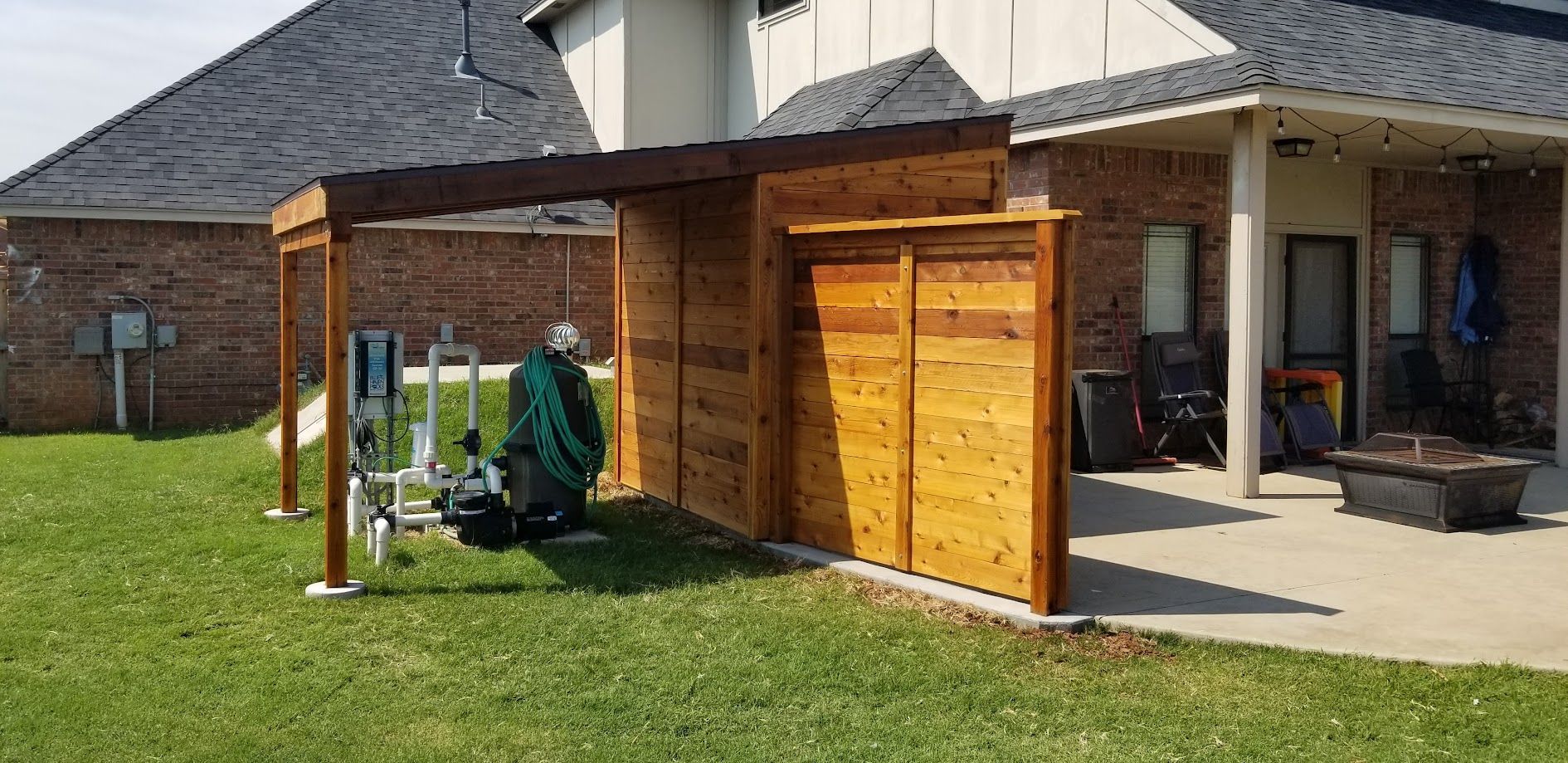 Wooden backyard pergola attached to a house, with a person mowing the lawn nearby.