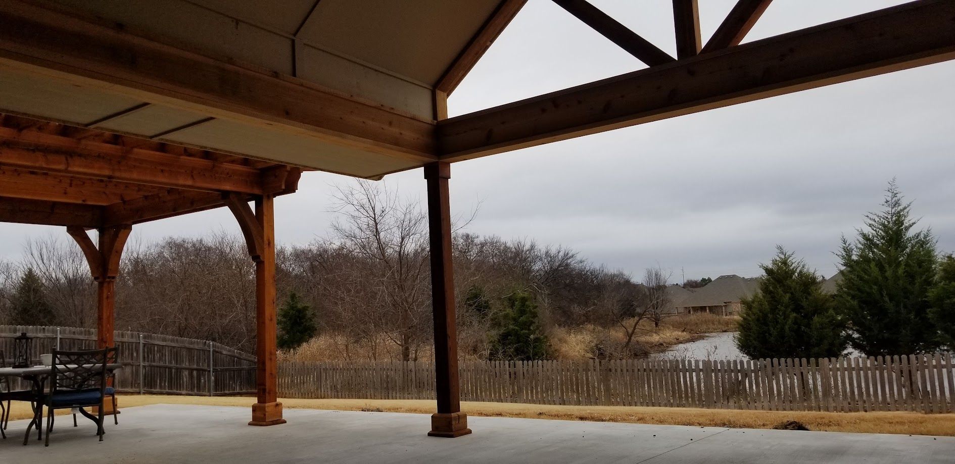 Covered patio overlooking a wintery yard with bare trees and a fence under a cloudy sky