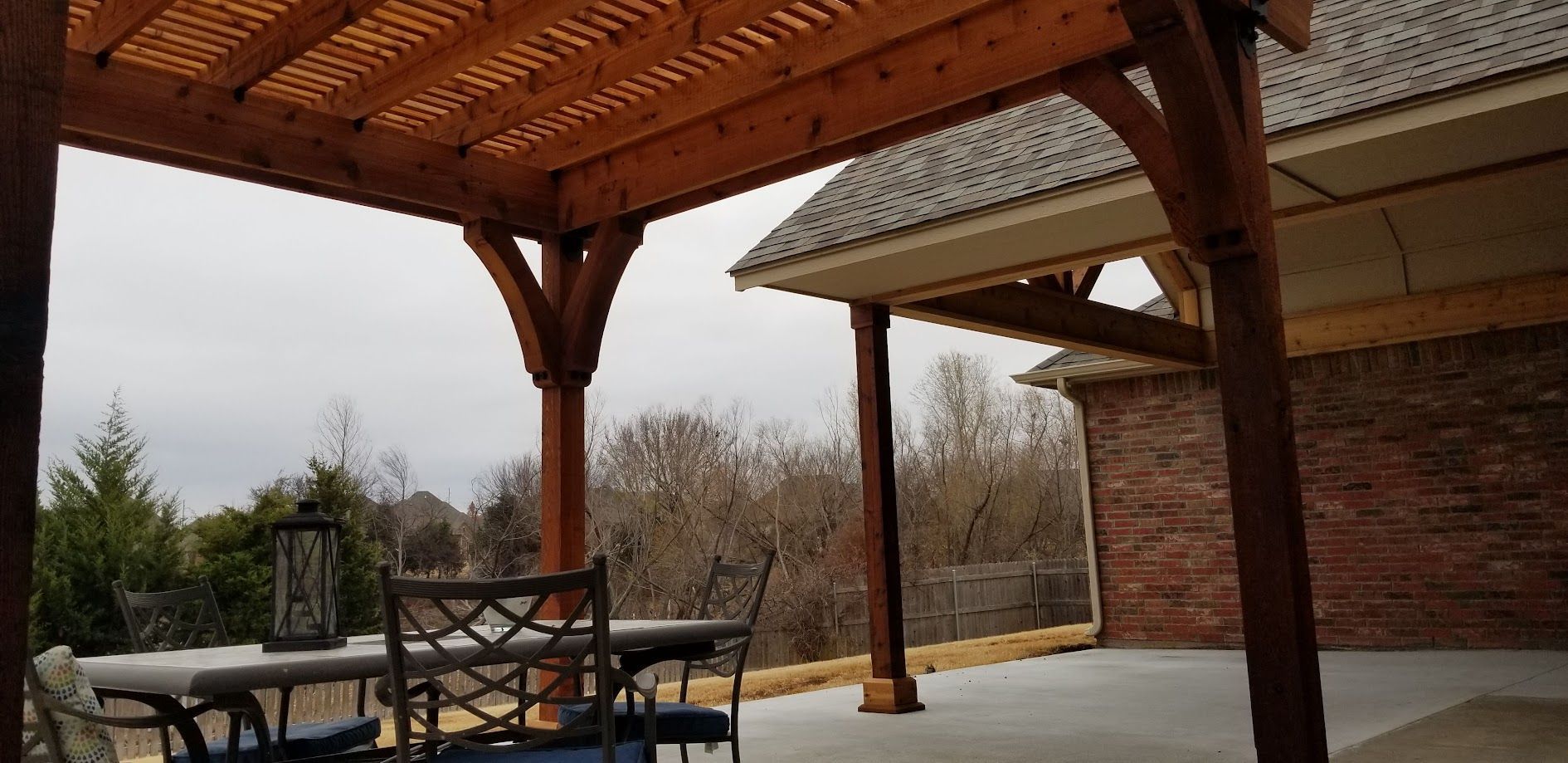 Covered patio with wooden beams, outdoor dining table and chairs, brick wall, and a snowy backyard view