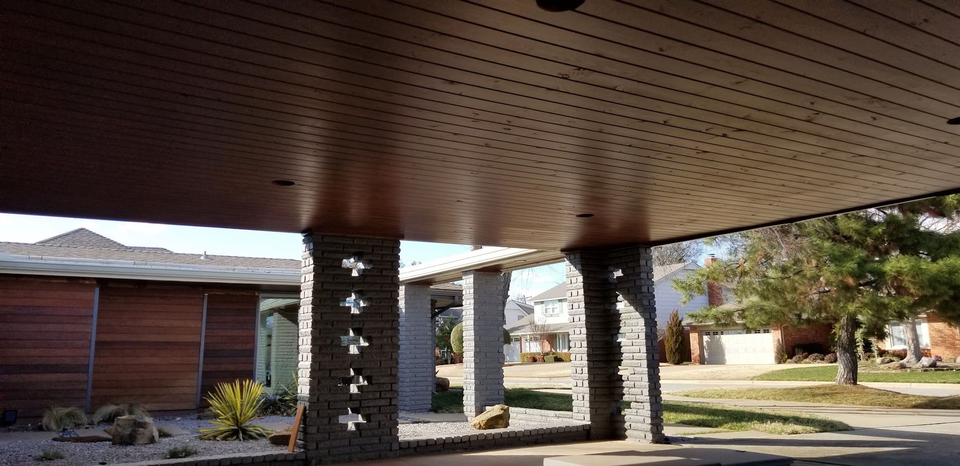 Covered outdoor walkway with brick columns, wood ceiling, and landscaped courtyard beyond