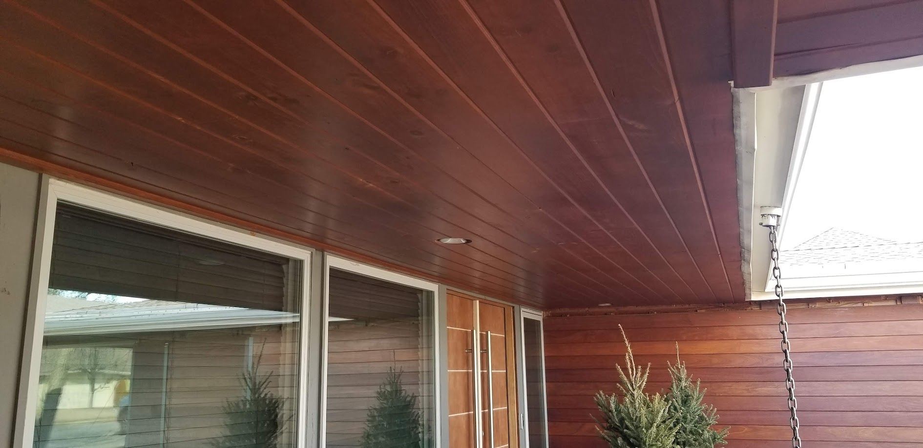 Wood-paneled porch ceiling with sliding glass doors and a small shrub beside a house exterior