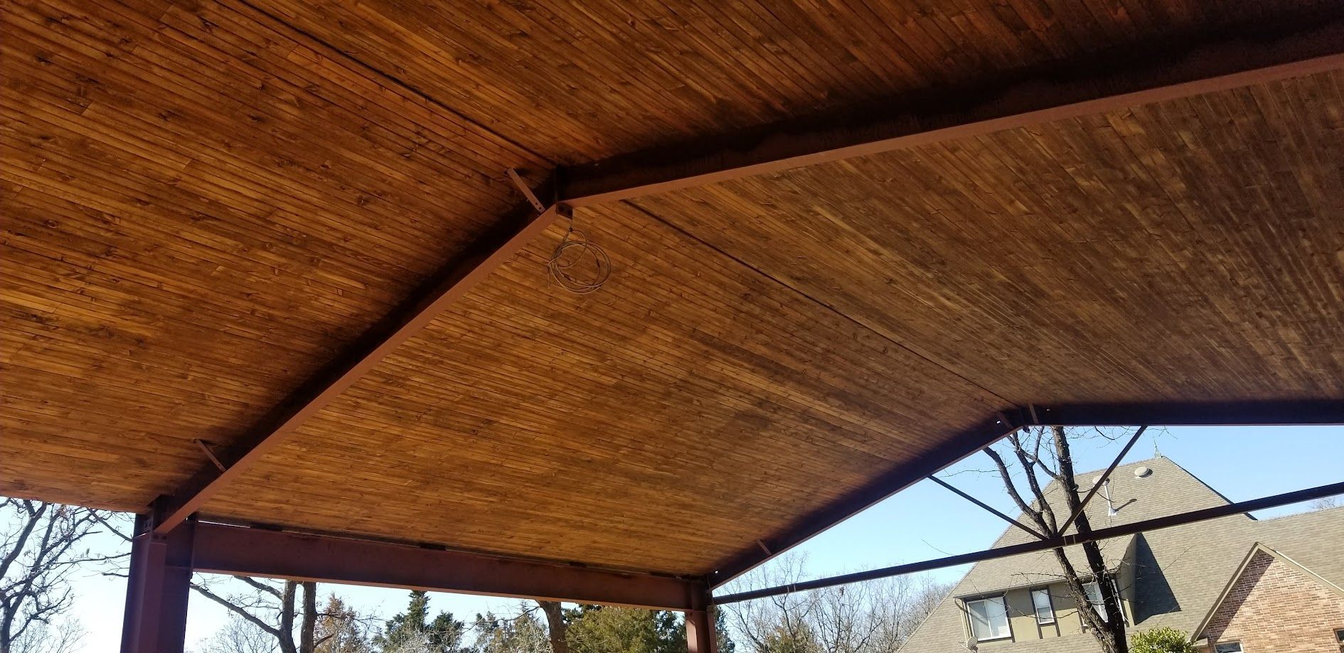 Wooden pavilion roof with beams, overlooking rooftops and trees on a sunny day