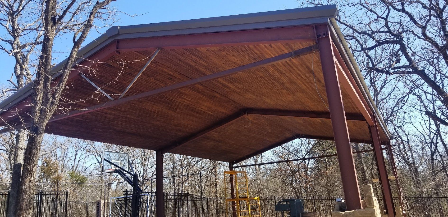 Wooden pavilion with a peaked roof in a park, viewed from below among bare trees